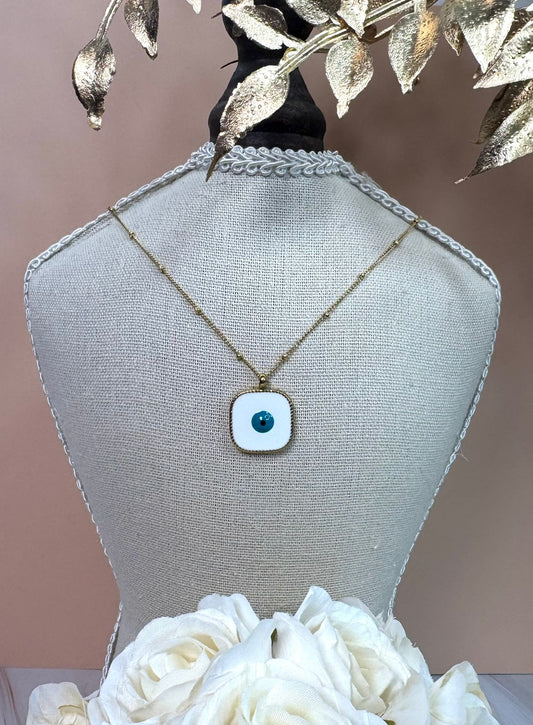 Necklace with a blue evil eye pendant on a mannequin bust with white flowers and gold leaves.